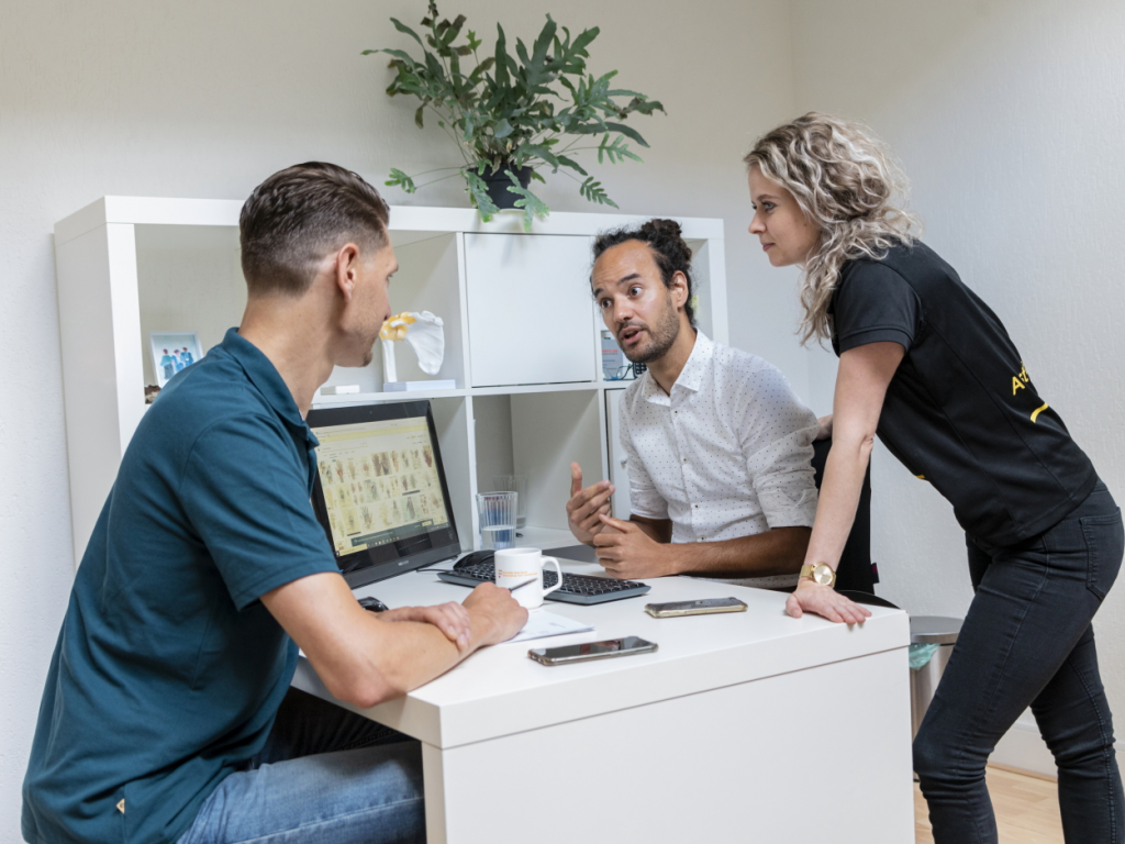 Drie personen kletsen aan tafel achter een computer