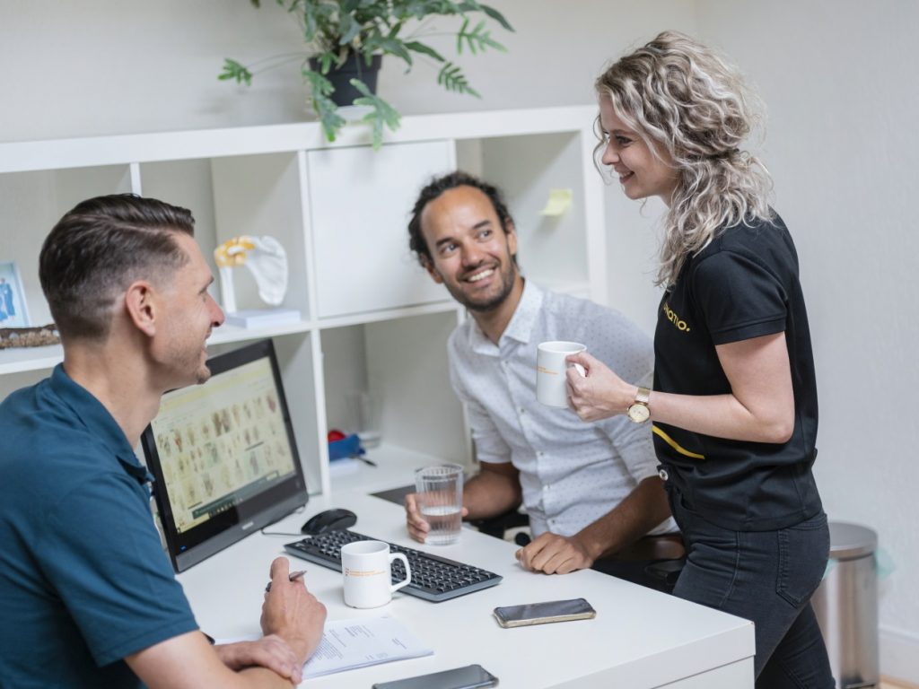 Drie mensen in gesprek aan een bureau met computer