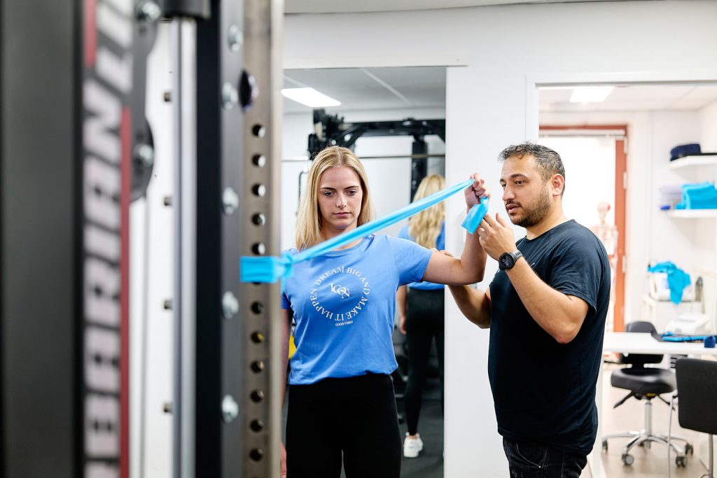 fysiotherapeut geeft instructies aan vrouw bij oefening met elastische band