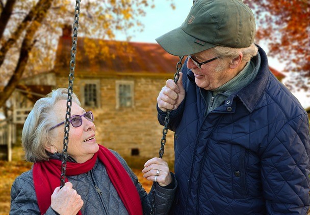 Oudere vrouw op een schommel kijkt naar oudere man met petje op