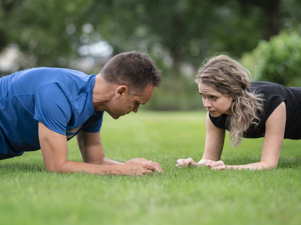 Man en vrouwen doen oefening planken in gras