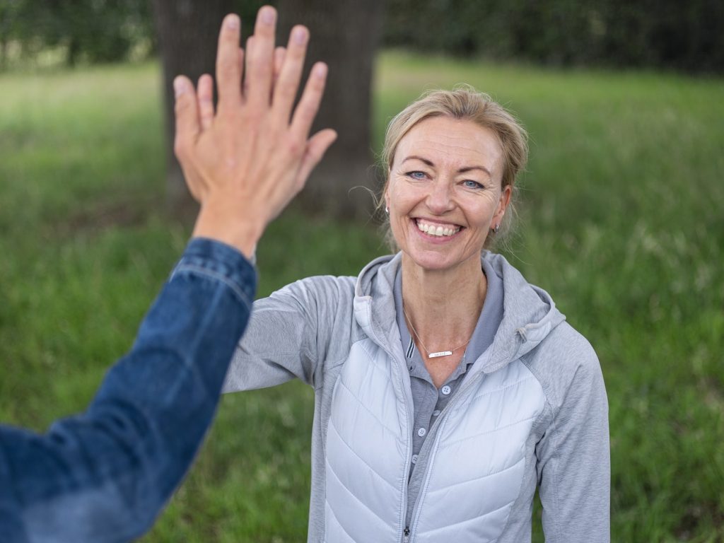 Vrouw in grijze jas geeft highfive